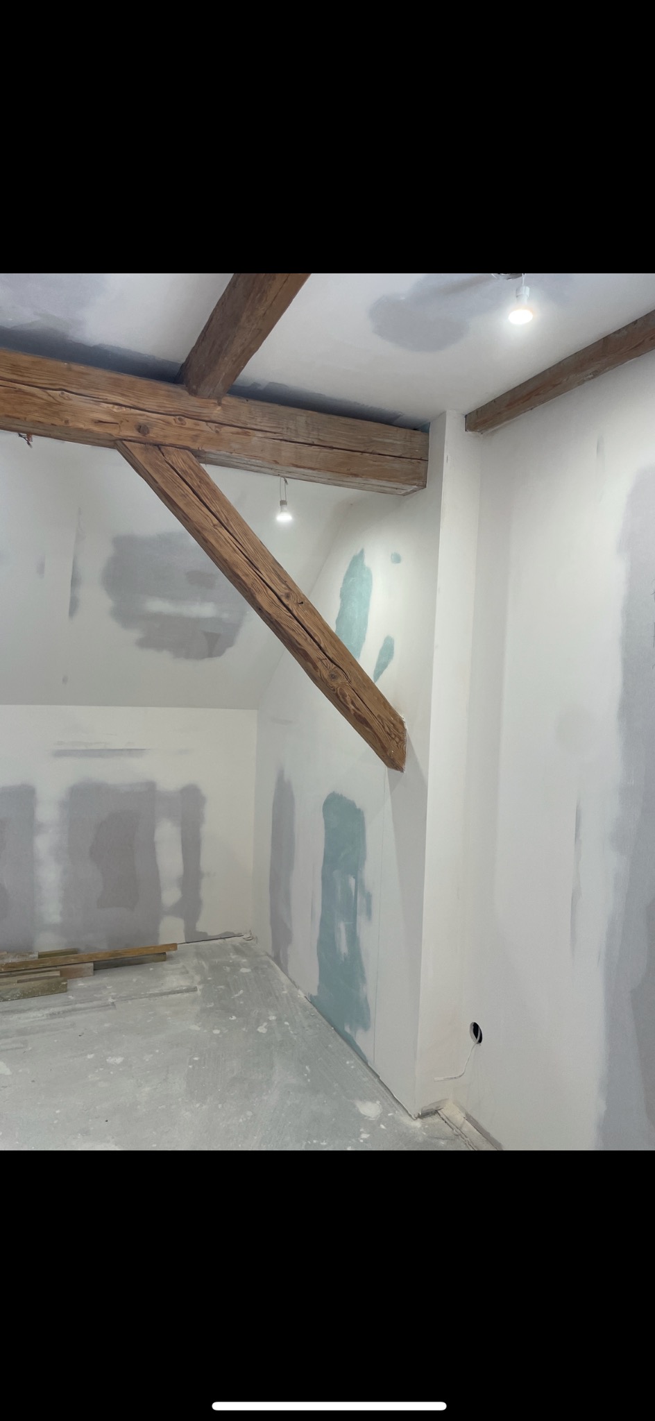 Wnętrze poddasza w Nowogrodźcu w trakcie prac wykończeniowych, z widocznymi drewnianymi belkami stropowymi, częściowo zagruntowanymi ścianami i przygotowanym podłożem pod dalsze prace.