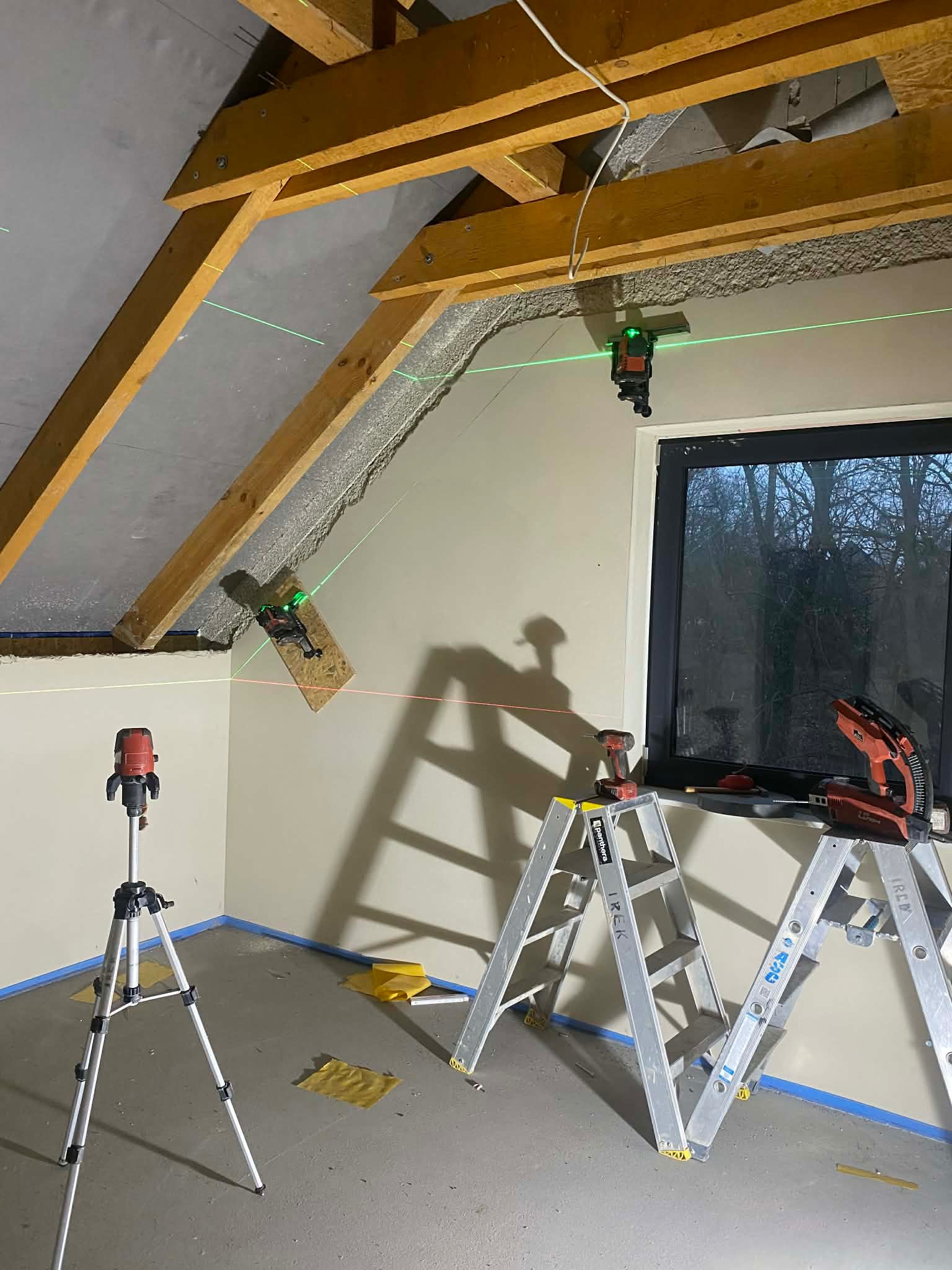 Skośne poddasze w trakcie prac wykończeniowych. Widoczne lasery krzyżowe, drabiny i narzędzia. Przygotowanie do montażu płyt.