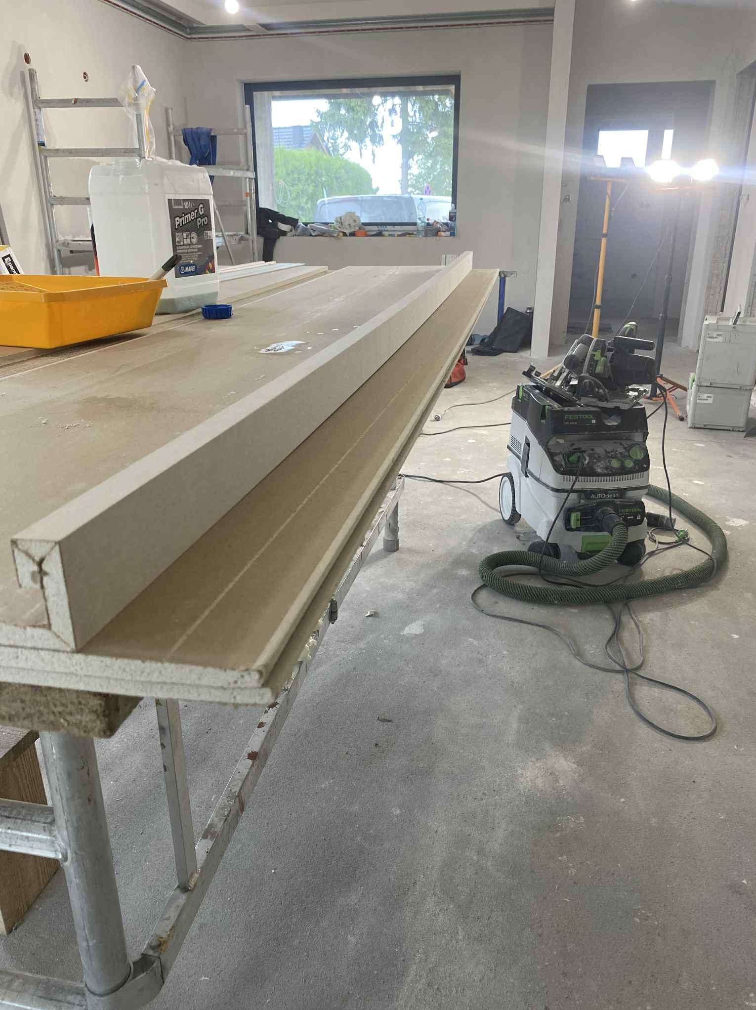 Przygotowane profile gipsowe na stole roboczym, widoczny odkurzacz przemysłowy Festool, wnętrze w trakcie prac wykończeniowych, okno w tle.