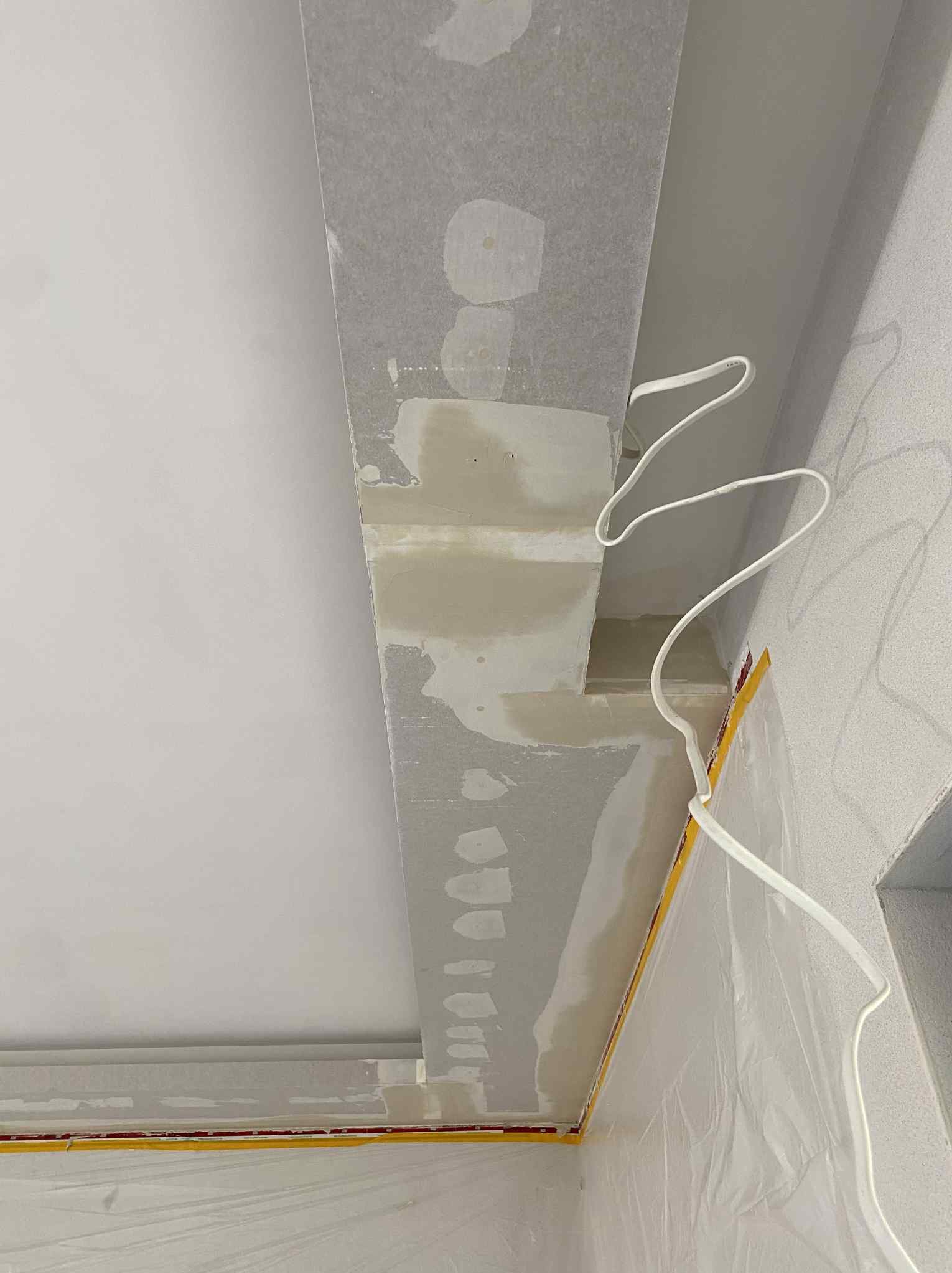 Sufit po szpachlowaniu z widocznymi przewodami elektrycznymi i zabezpieczeniem folią malarską. Widok z dołu, jasne oświetlenie.