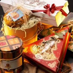 Zestaw świąteczny upominkowy: ciasto Panettone w okrągłym pudełku, piernik w opakowaniu w kształcie choinki, puszka z babą drożdżową i kartonowe pudełka z kokardami, wszystko marki Consonni.