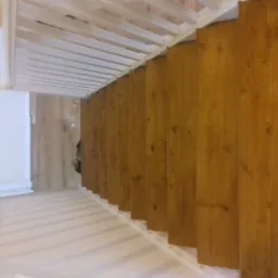 Drewniane schody z białymi barierkami, widok z góry, jasne drewno, białe ściany w tle.