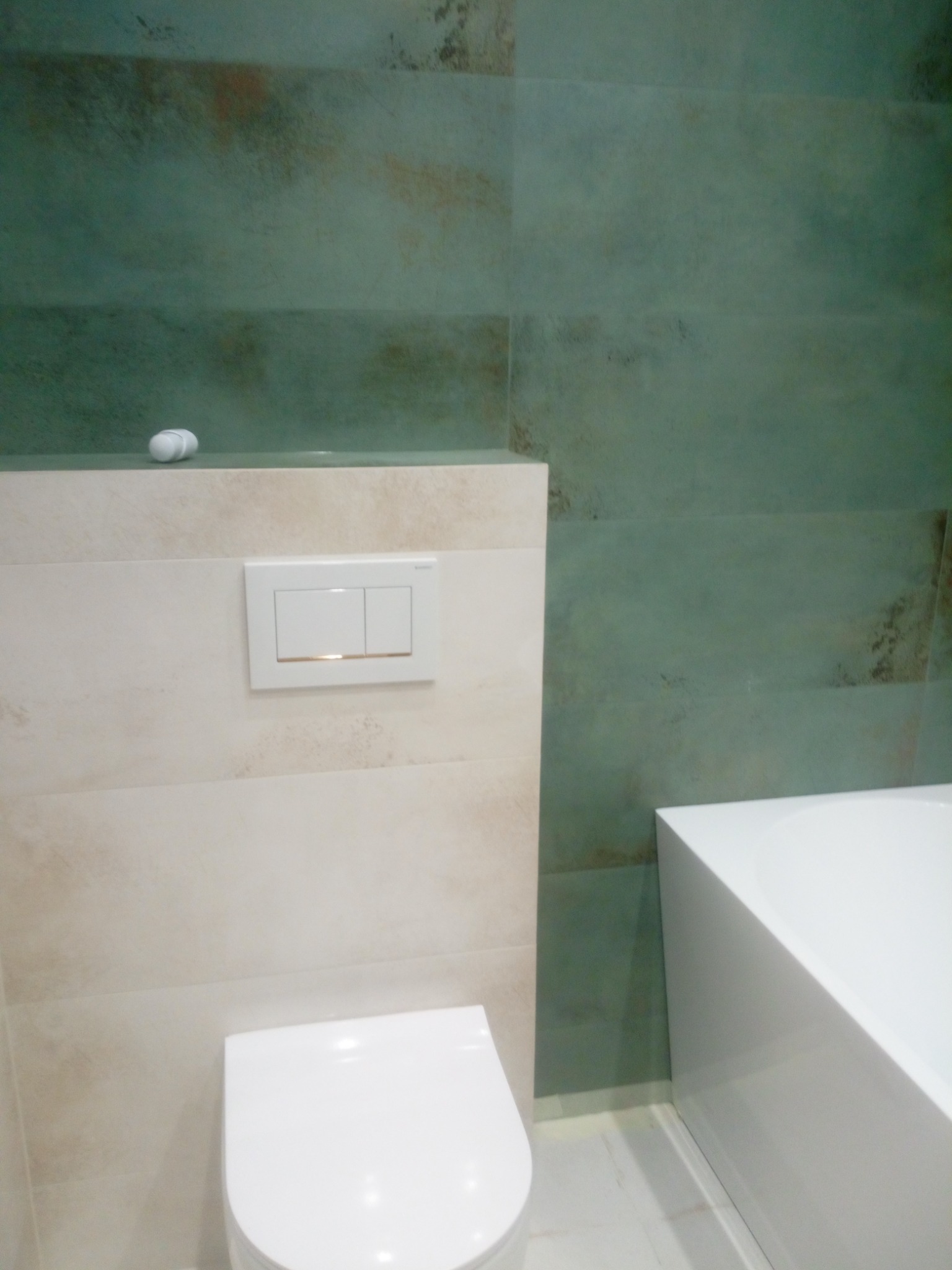 Nowoczesna łazienka z wiszącą toaletą, beżowymi i zielonymi płytkami imitującymi kamień, oraz białą wanną narożną.