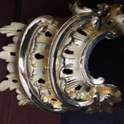 Złocona, dekoracyjna rozeta architektoniczna z ornamentami roślinnymi, widoczna z bliska na ciemnym tle.