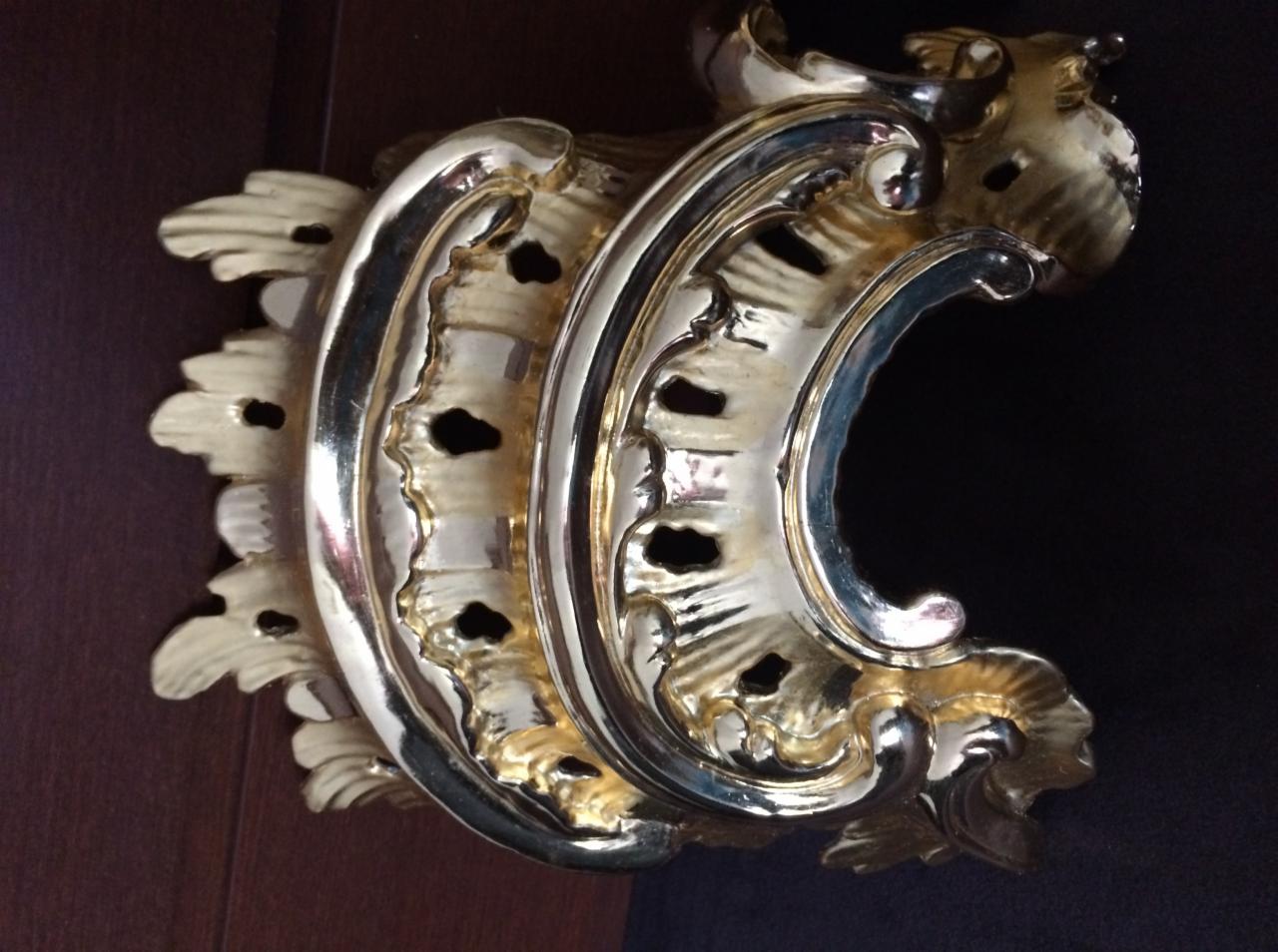 Złocona, dekoracyjna rozeta architektoniczna z ornamentami roślinnymi, widoczna z bliska na ciemnym tle.