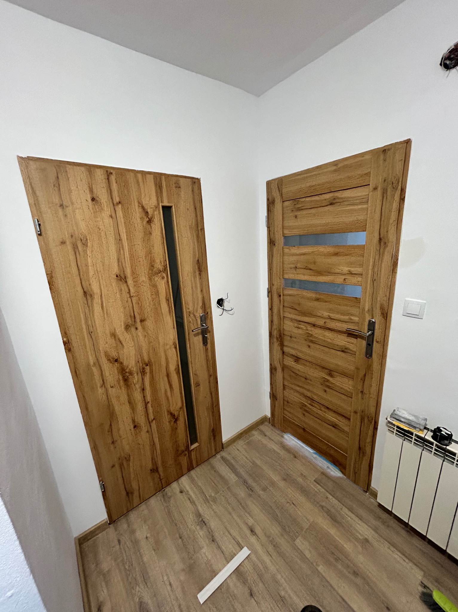 Dwa drewniane drzwi wewnętrzne z przeszkleniami, zamontowane w nowym mieszkaniu z panelami podłogowymi, widoczne ślady po pracach wykończeniowych.