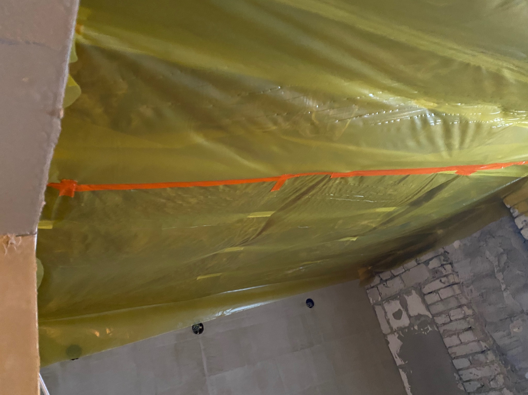 Wnętrze w trakcie zabezpieczania folią malarską przed pracami wykończeniowymi, widoczne zaklejone otwory na gniazdka elektryczne i fragment ściany z cegły.