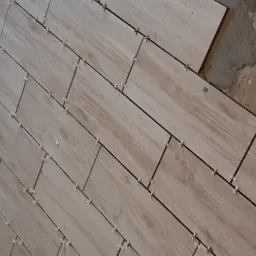 Ułożone płytki podłogowe imitujące drewno, z widocznymi krzyżykami dystansowymi i fragmentem nieprzygotowanej ściany.