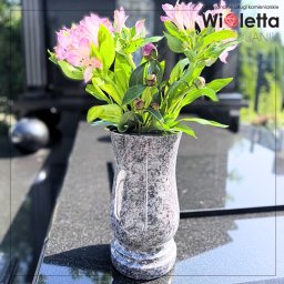 Usługi Kamieniarskie Janik Wioletta - Granitowy wazon nagrobny z kwiatami na wypolerowanym, czarnym nagrobku. Stonowana kolorystyka, miękkie światło, minimalistyczny charakter.