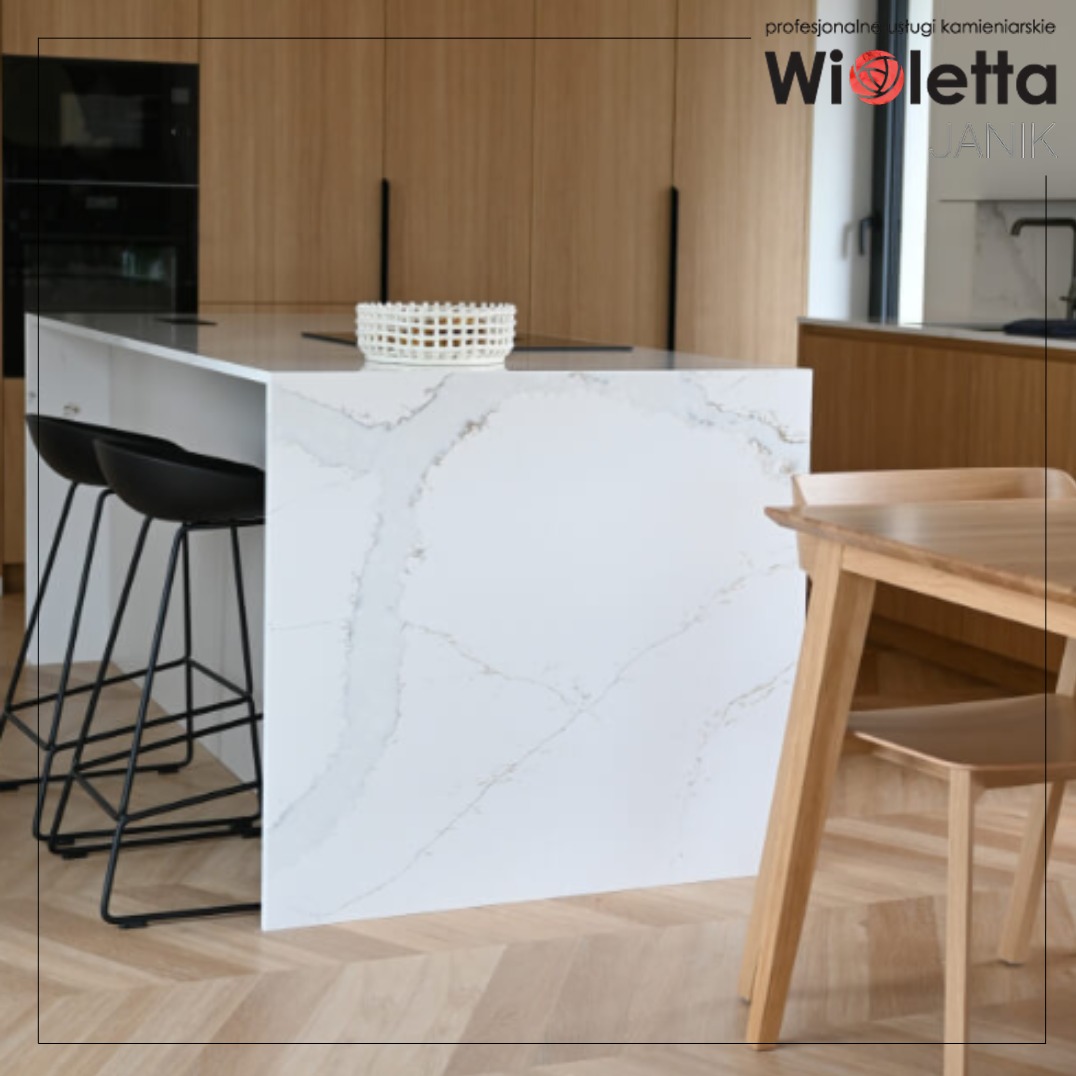 Biała wyspa kuchenna ze spieku kwarcowego z widocznym marmurkowym wzorem, czarne hokery, drewniana podłoga i stół. Nowoczesna kuchnia w jasnych barwach.