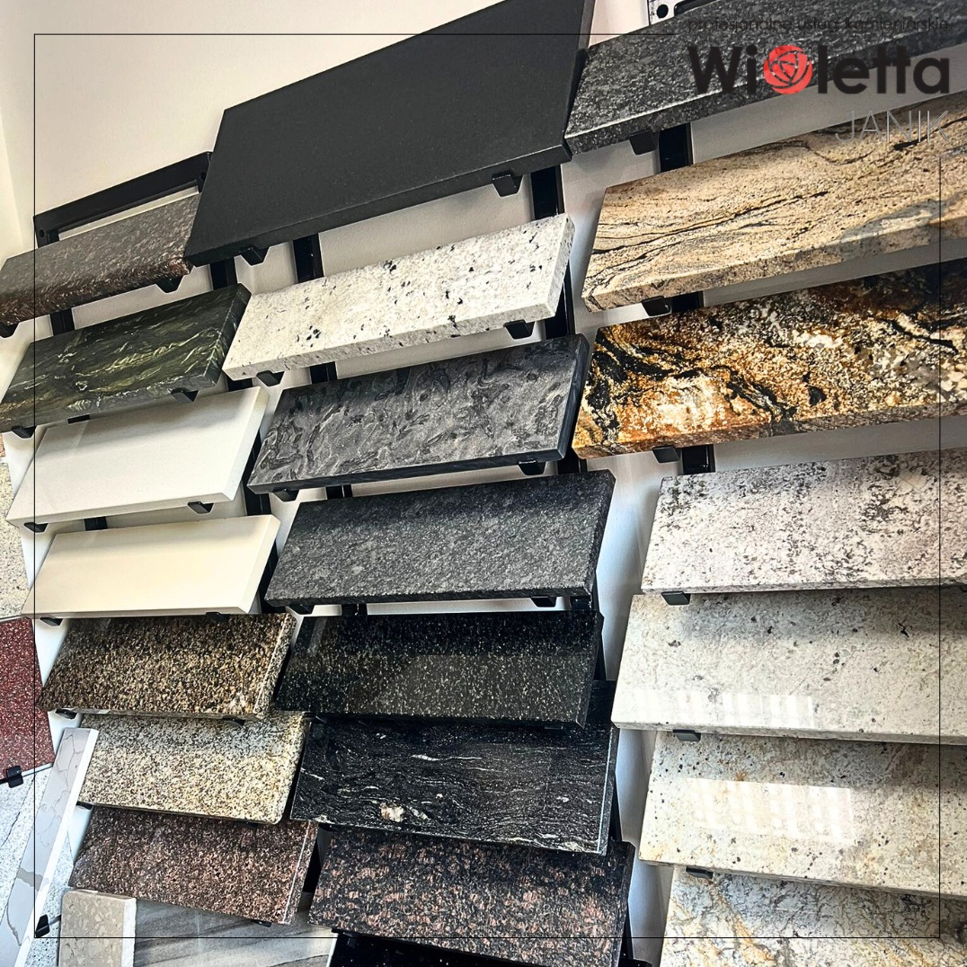 Ekspozycja różnorodnych próbek kamiennych blatów (granit, marmur) o bogatej kolorystyce i wzornictwie, zamontowanych na metalowym stelażu w pionie.