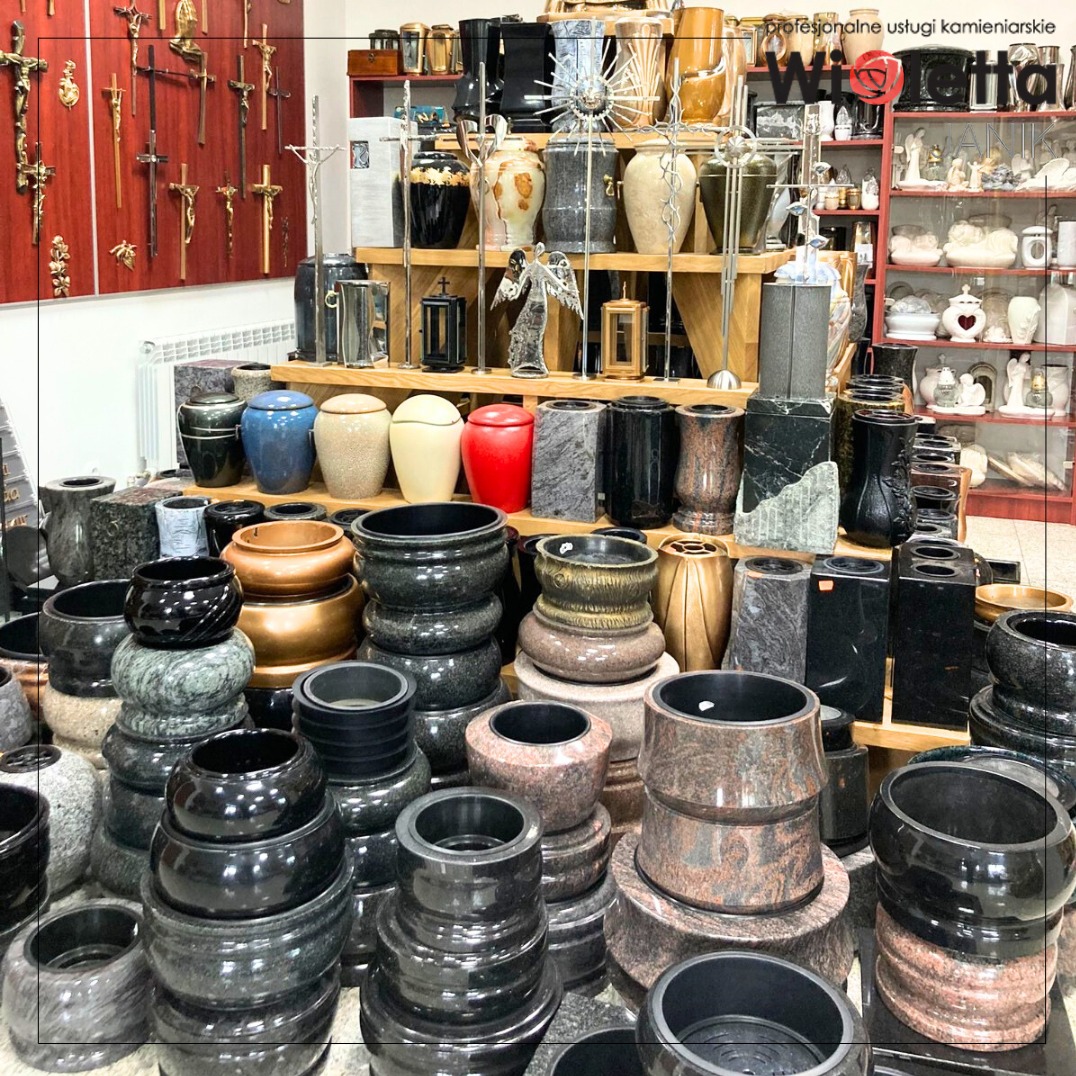 Ekspozycja urn i wazonów nagrobnych z kamienia w różnych kolorach i kształtach, ustawionych na półkach i podłodze w sklepie kamieniarskim.