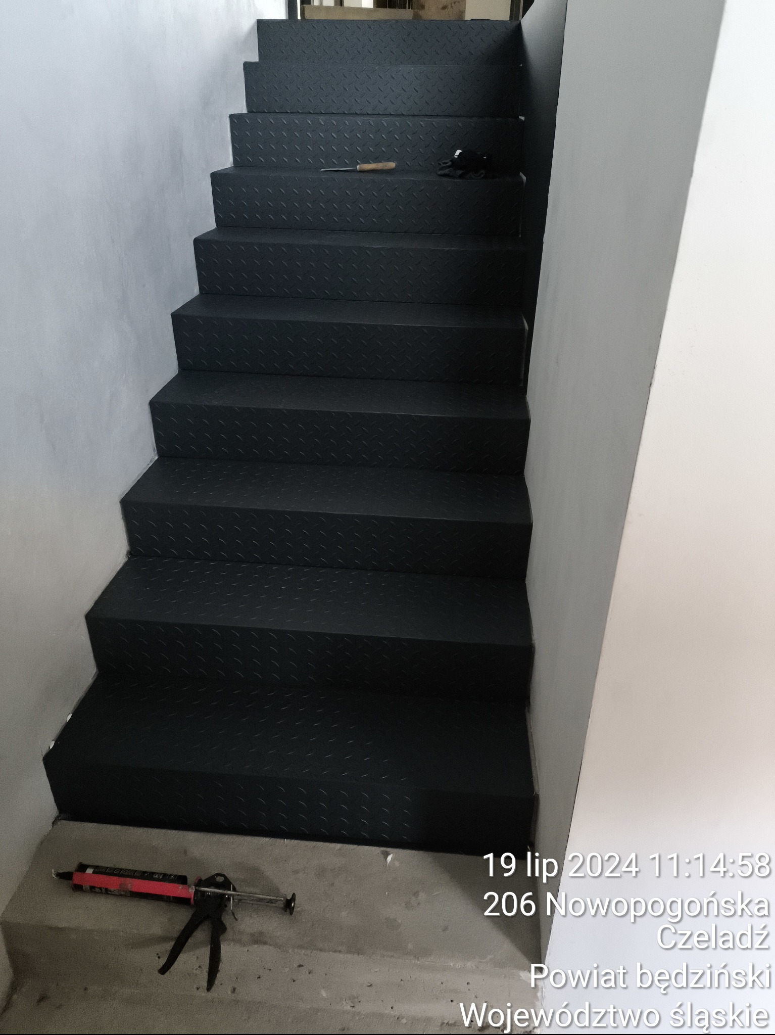 Czarne, metalowe schody z blachy ryflowanej w klatce schodowej, widoczne narzędzia: pistolet do silikonu i nóż.