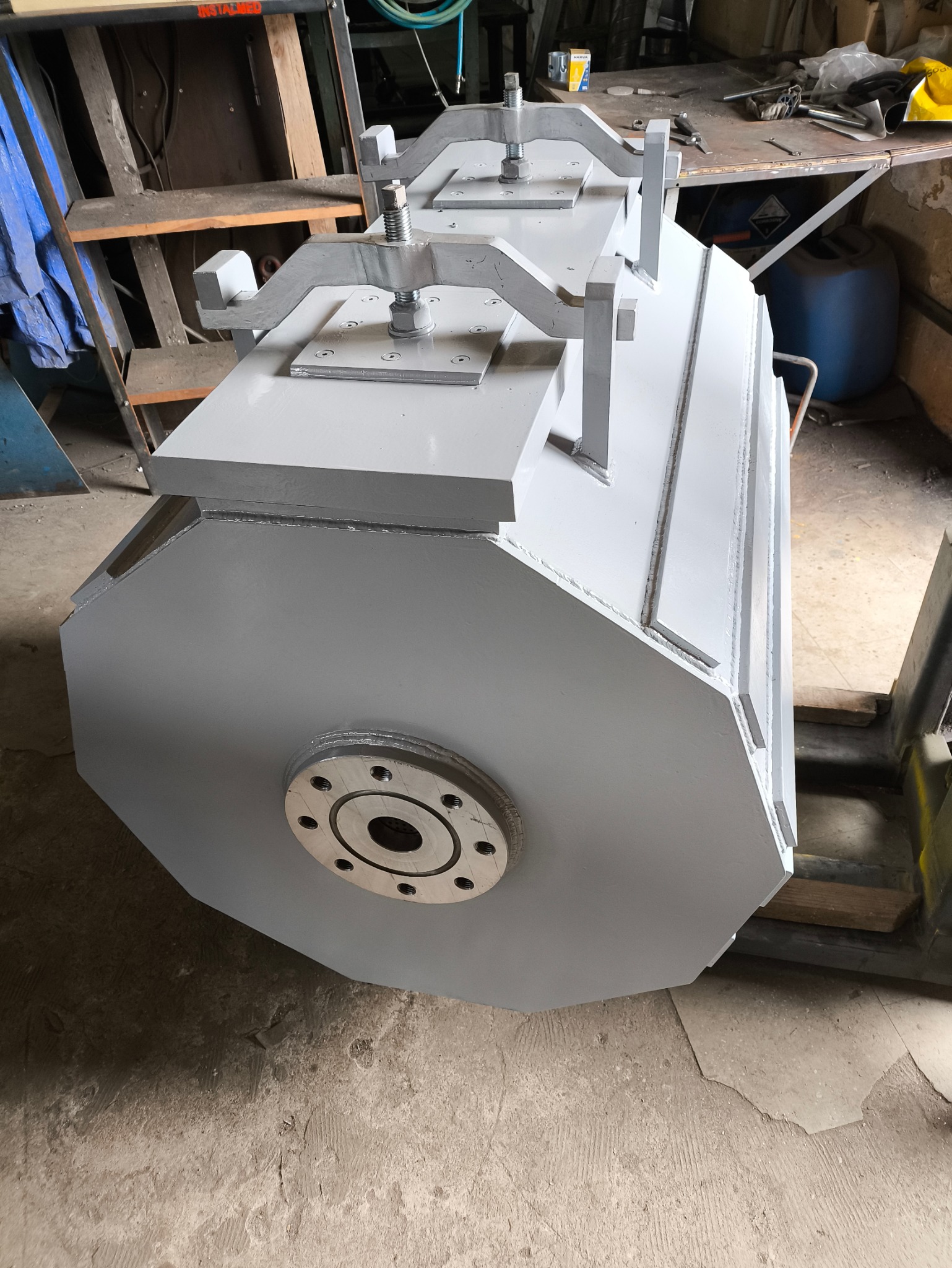 Szara, metalowa konstrukcja z elementami zespawanymi, widoczne spawy, nakrętki i śruby, na tle warsztatu.