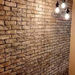 Dekoracyjna ściana z cegły w odcieniach brązu, oświetlona trzema lampami wiszącymi z czarnymi, geometrycznymi kloszami i żarówkami Edison, tworząca nowoczesny design wnętrza.