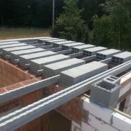 Wieniec stropowy z prefabrykatów betonowych na murach z cegły kratówki, widok z góry na budowę domu jednorodzinnego, w tle drzewa.