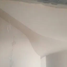 Gładko wykończona ściana i sufit po nałożeniu gładzi, z widocznymi przewodami elektrycznymi wystającymi ze ściany.