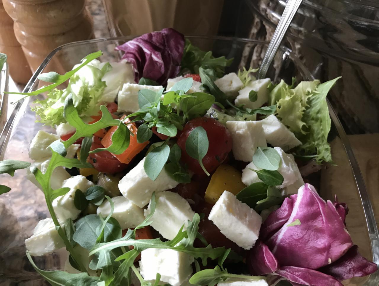 Szklana misa z sałatką caprese z pomidorkami koktajlowymi, serem feta, rukolą i świeżymi ziołami, przygotowaną w Pruszkowie.