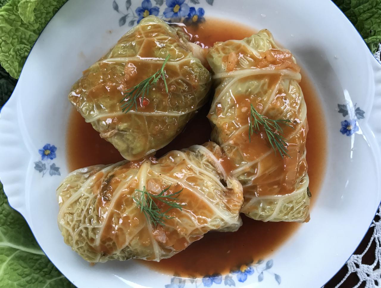 Trzy gołąbki z kapusty włoskiej w sosie pomidorowym, udekorowane gałązkami kopru na talerzu w niebieskie kwiatki.