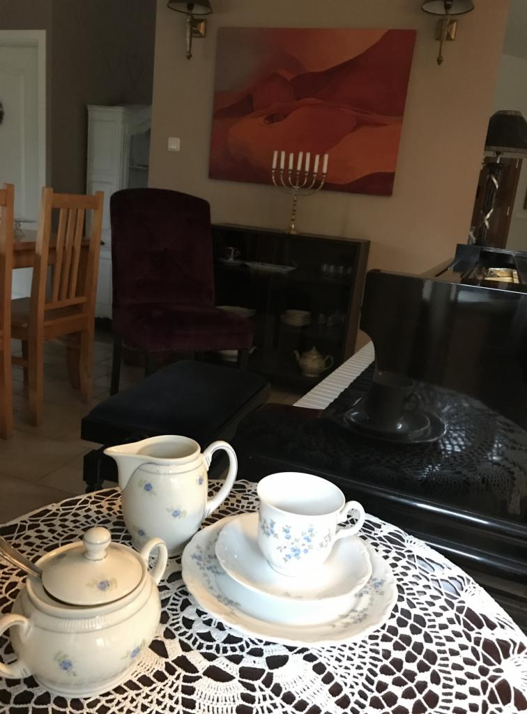 Porcelanowy serwis do herbaty w niebieskie kwiatki, ustawiony na koronkowej serwecie, z pianinem w tle.