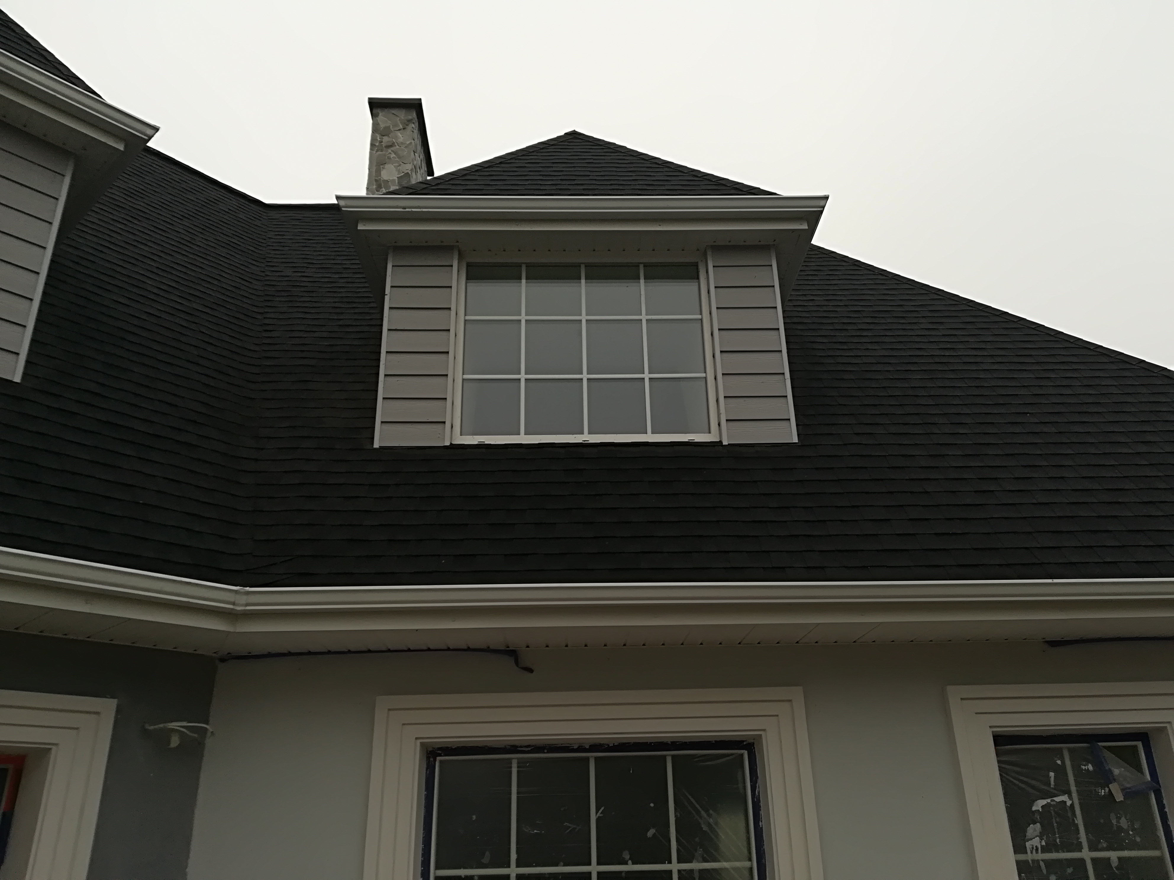 Dom z czarnym dachem i szarymi panelami bocznymi okna na poddaszu, okna na parterze zabezpieczone folią malarską.