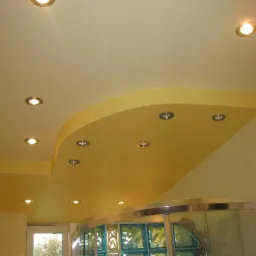 Żółty, podwieszany sufit z wbudowanymi punktowymi lampami LED nad kabiną prysznicową z luksferami.