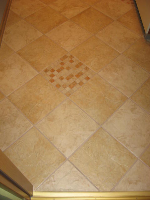 Ułożona podłoga z beżowych, kwadratowych płytek ułożonych romboidalnie z dekoracyjnym wzorem z mniejszych płytek w centrum, widok z góry.