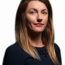 Portret kobiety z brązowymi włosami i w granatowej sukience z ozdobnym dekoltem, uśmiechająca się lekko do kamery na białym tle.