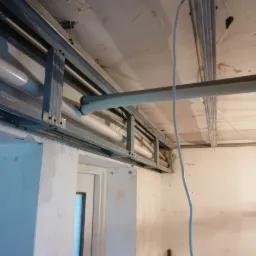 Stelaż metalowy sufitu podwieszanego z widocznymi rurami i przewodami elektrycznymi, surowy stan wykończenia wnętrza.