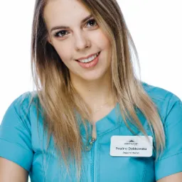 Portret uśmiechniętej kobiety w turkusowym uniformie z identyfikatorem 'Petrosjan Clinic' i imieniem 'Paulina Dobkowska', skrzyżowane ręce, manicure hybrydowy.