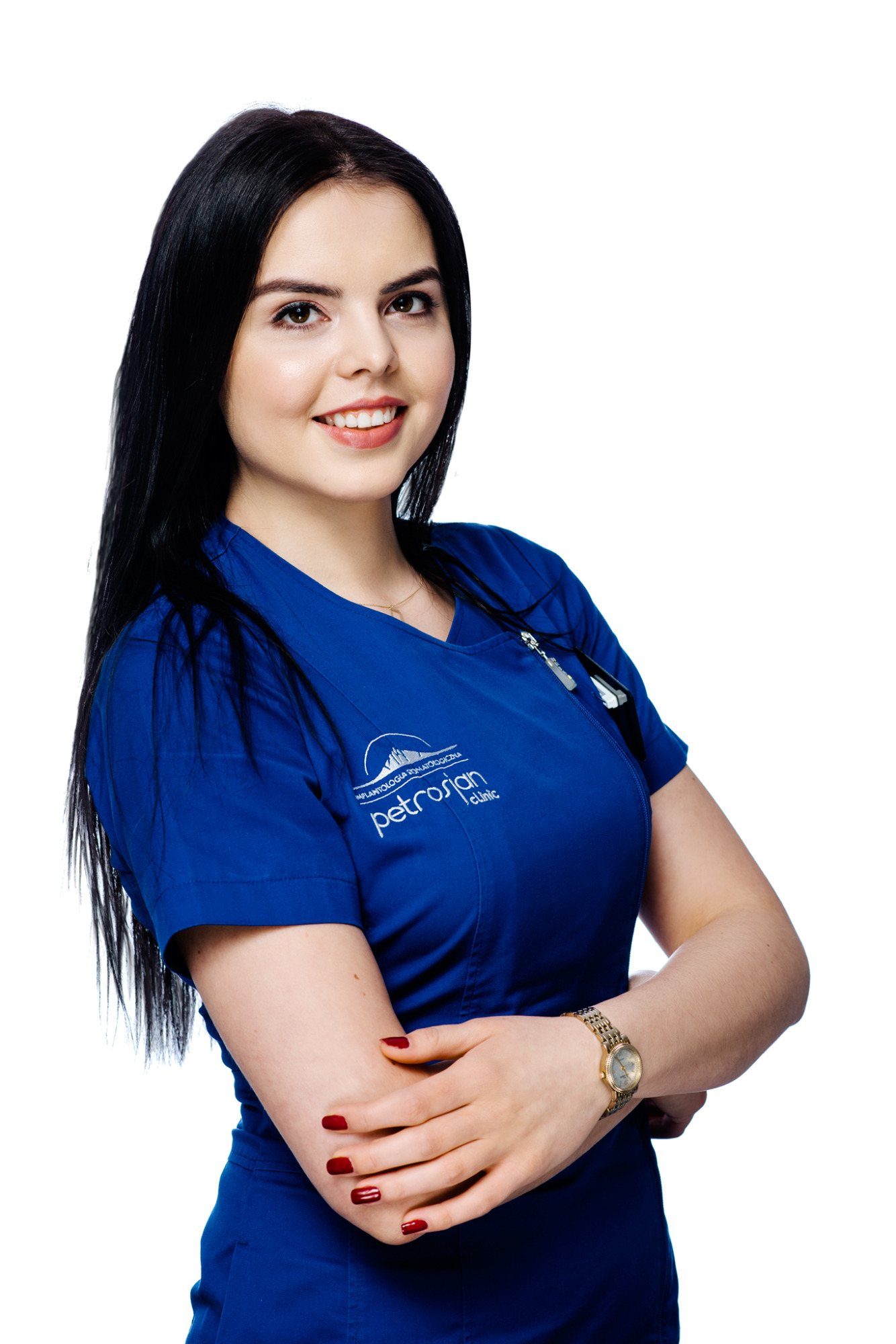 Portret uśmiechniętej brunetki w niebieskim uniformie medycznym z logo kliniki 'Petrosian', z zegarkiem na ręce i czerwonym manicure na białym tle.