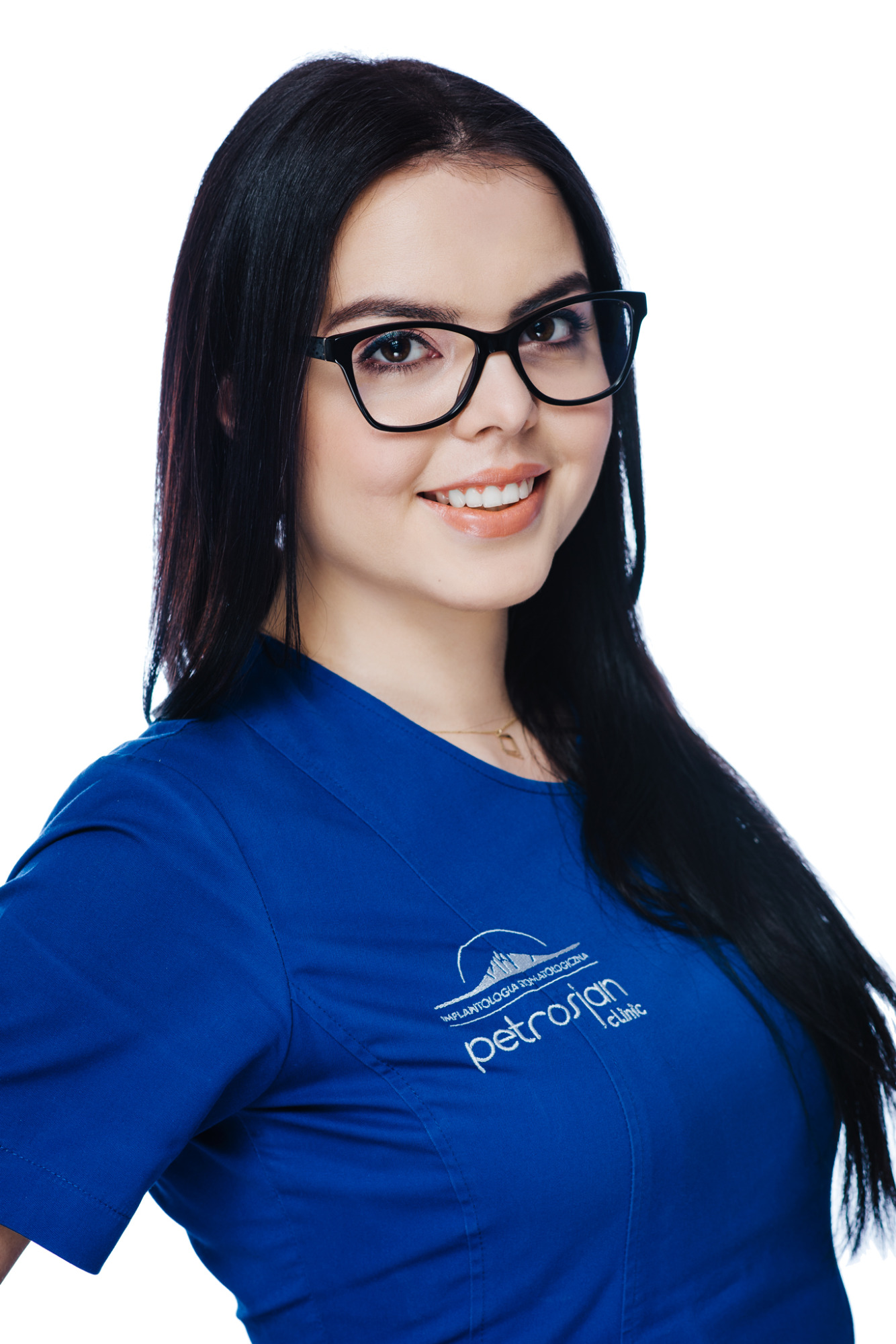 Portret uśmiechniętej kobiety w okularach i niebieskim uniformie z logo kliniki implantologii dentystycznej.