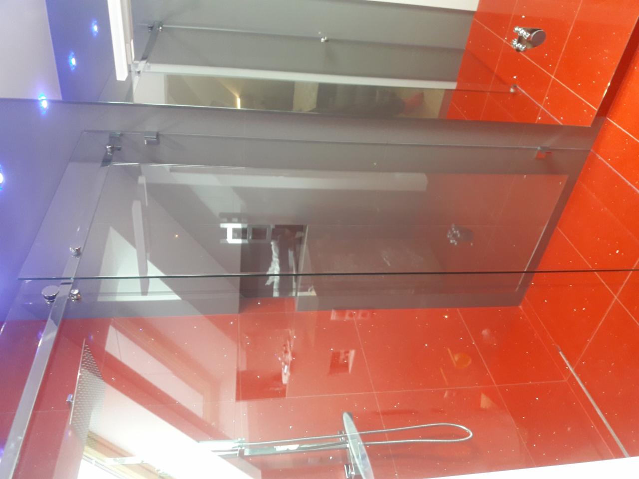 Szklana kabina prysznicowa z chromowanymi okuciami i czerwonymi płytkami na ścianach i podłodze.