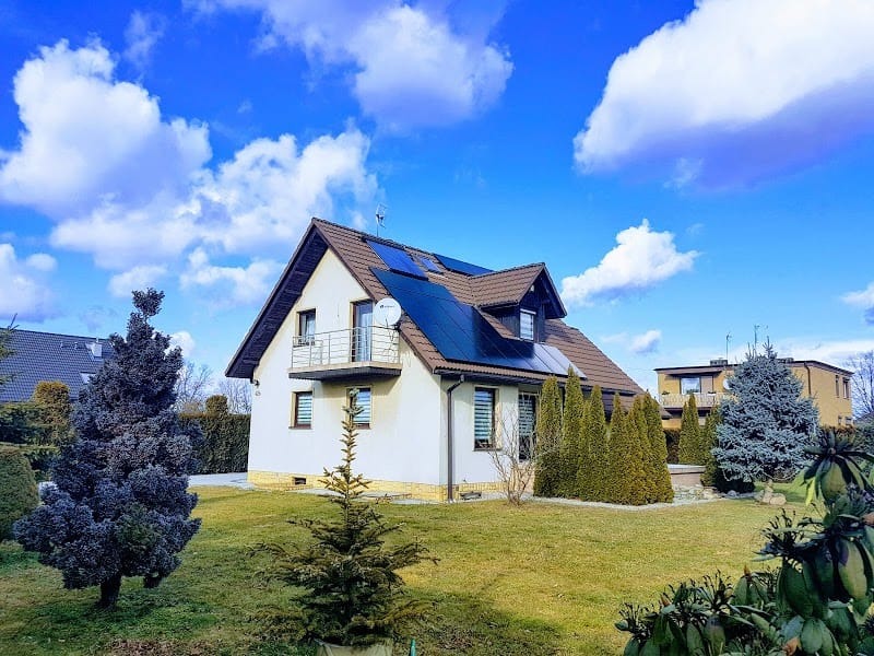 Dom jednorodzinny z brązowym dachem i panelami słonecznymi, widok z ogrodu w słoneczny dzień.