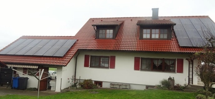 Dom jednorodzinny z czerwoną dachówką i panelami słonecznymi na dachu, widok z przodu w pochmurny dzień.