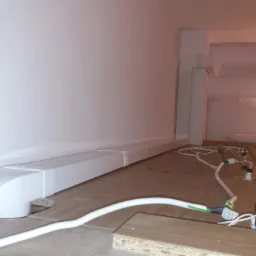 Instalacja elektryczna pod szafkami kuchennymi z widocznymi kablami, puszkami i listwą przypodłogową z kanałem kablowym w tle.