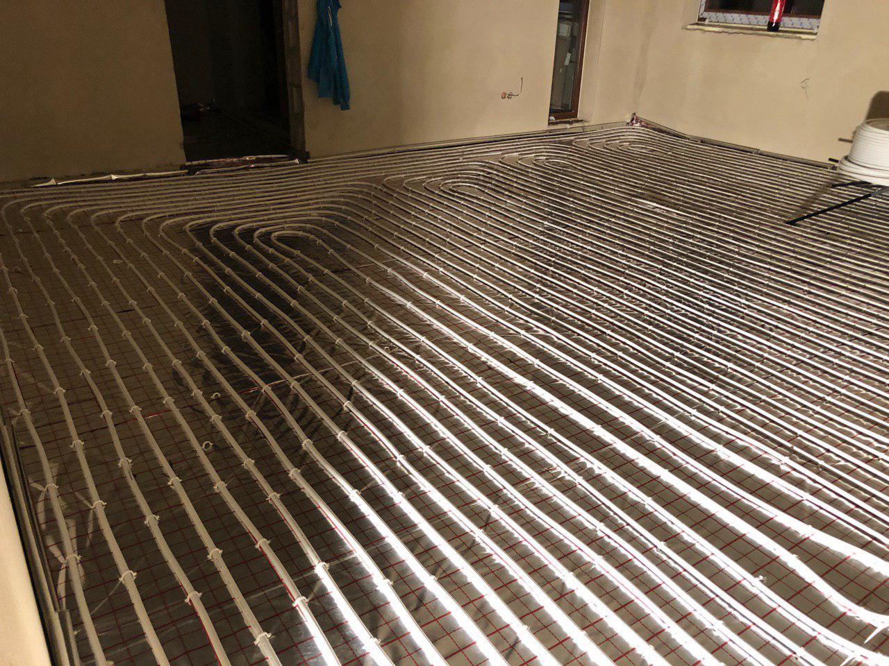 Rozłożona instalacja ogrzewania podłogowego na folii z czerwoną siatką, widok z góry, przygotowanie do zalania wylewką.