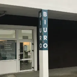 Wejście do biura z kolumnami oznaczonymi napisami 'BIURO' i 'RACHUNKOWE', widoczna tabliczka z adresem 'Stowarzyszenie Akademia Rozwoju Ekonomii Społecznej'.