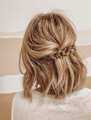 Fryzura z upięciem z tyłu głowy, spięta klamrą w panterkę, na tle beżowej ściany.