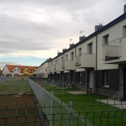 Słowiński Usługi Budowlane Michał Słowiński - Szereg nowych domów z balkonami, świeżo założone trawniki, ogrodzenie panelowe, pochmurne niebo.