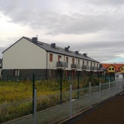 Słowiński Usługi Budowlane Michał Słowiński - Szereg domów jednorodzinnych z ciemnymi dachami i jasną elewacją, widocznych zza ogrodzenia w pochmurny dzień.