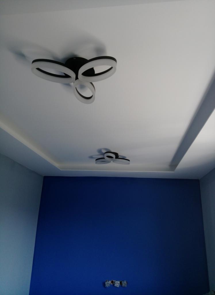 Nowoczesne oświetlenie sufitowe LED w kształcie pierścieni w nowo pomalowanym pokoju z niebieskimi ścianami i białym sufitem podwieszanym.