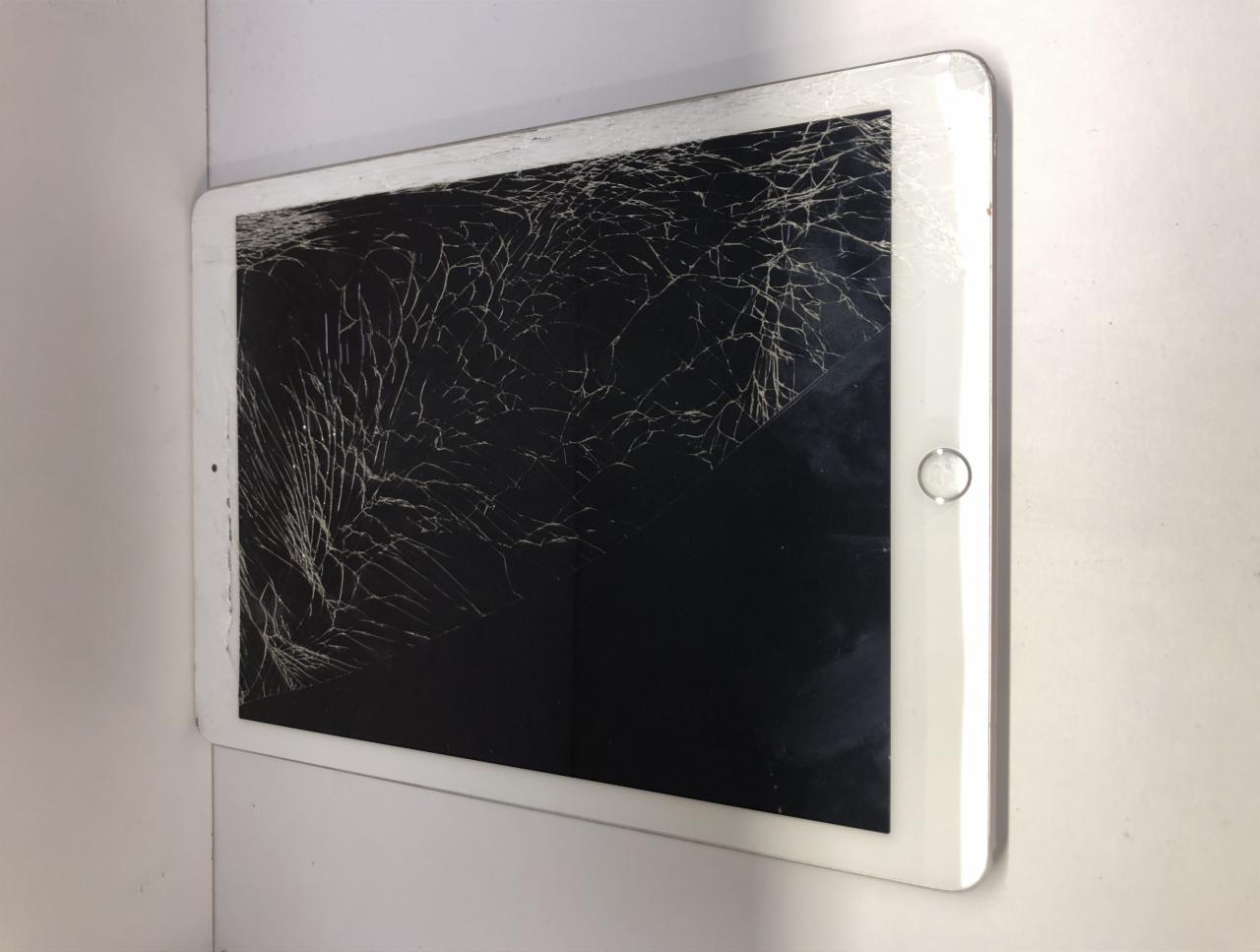 Biały tablet z pękniętym ekranem, widoczne liczne pajęczynowate pęknięcia szkła na czarnym tle wyłączonego wyświetlacza.