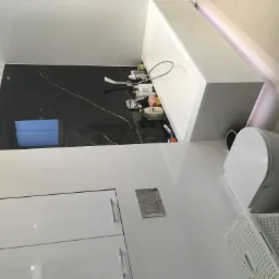 Nowoczesna łazienka z białą armaturą, czarną ścianą z marmurowym wzorem i białymi szafkami; widoczna wanna z kosmetykami, wisząca toaleta i kosz na pranie.