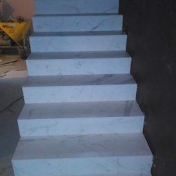 M.S KaFelki - Schody wyłożone białym marmurem z szarymi żyłami, widoczne narzędzia i resztki zaprawy w tle.