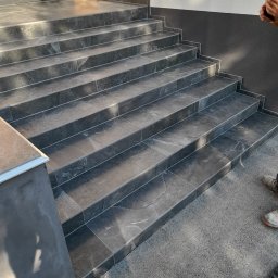 M.S KaFelki - Zewnętrzne schody wyłożone szarymi płytkami imitującymi kamień, z aluminiowymi listwami wykończeniowymi na krawędziach stopni.