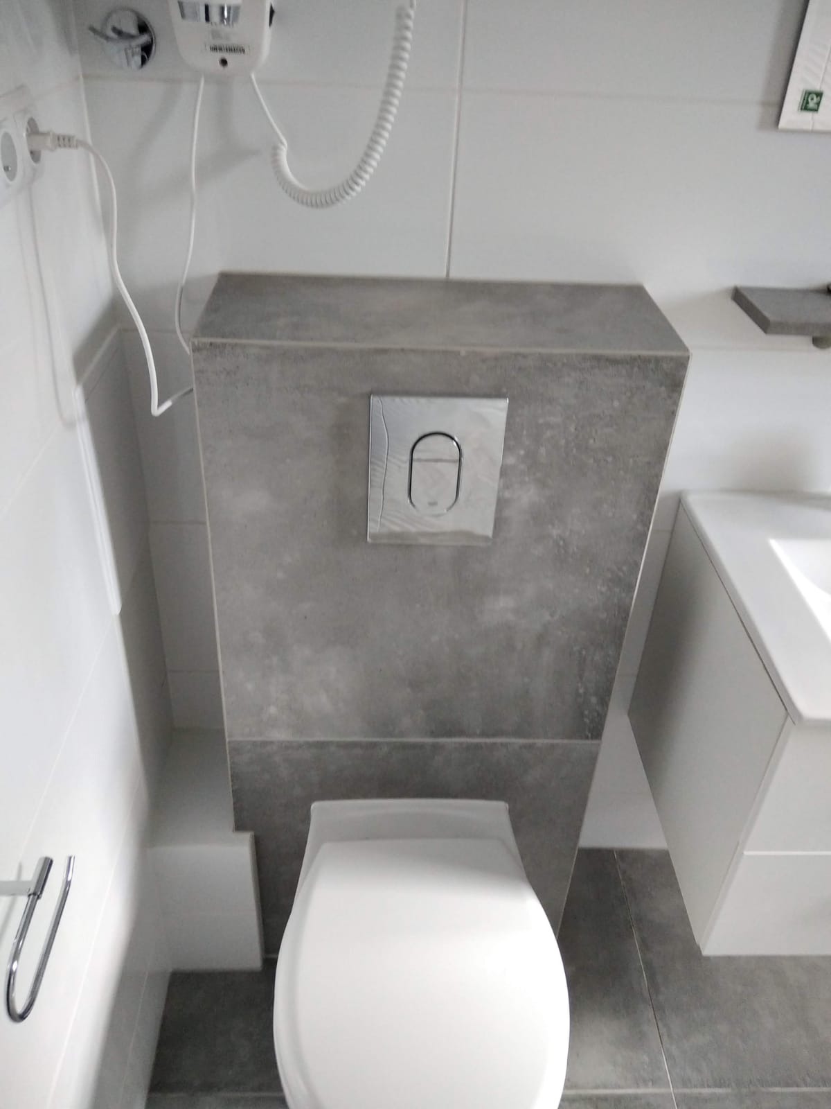 Nowoczesna toaleta z szarą obudową spłuczki w minimalistycznej łazience z białymi płytkami.