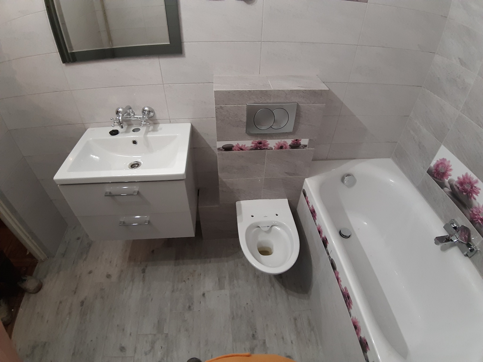 Jasna łazienka po remoncie: umywalka z szafką, toaleta i wanna z kwiatowym motywem dekoracyjnym na kafelkach.