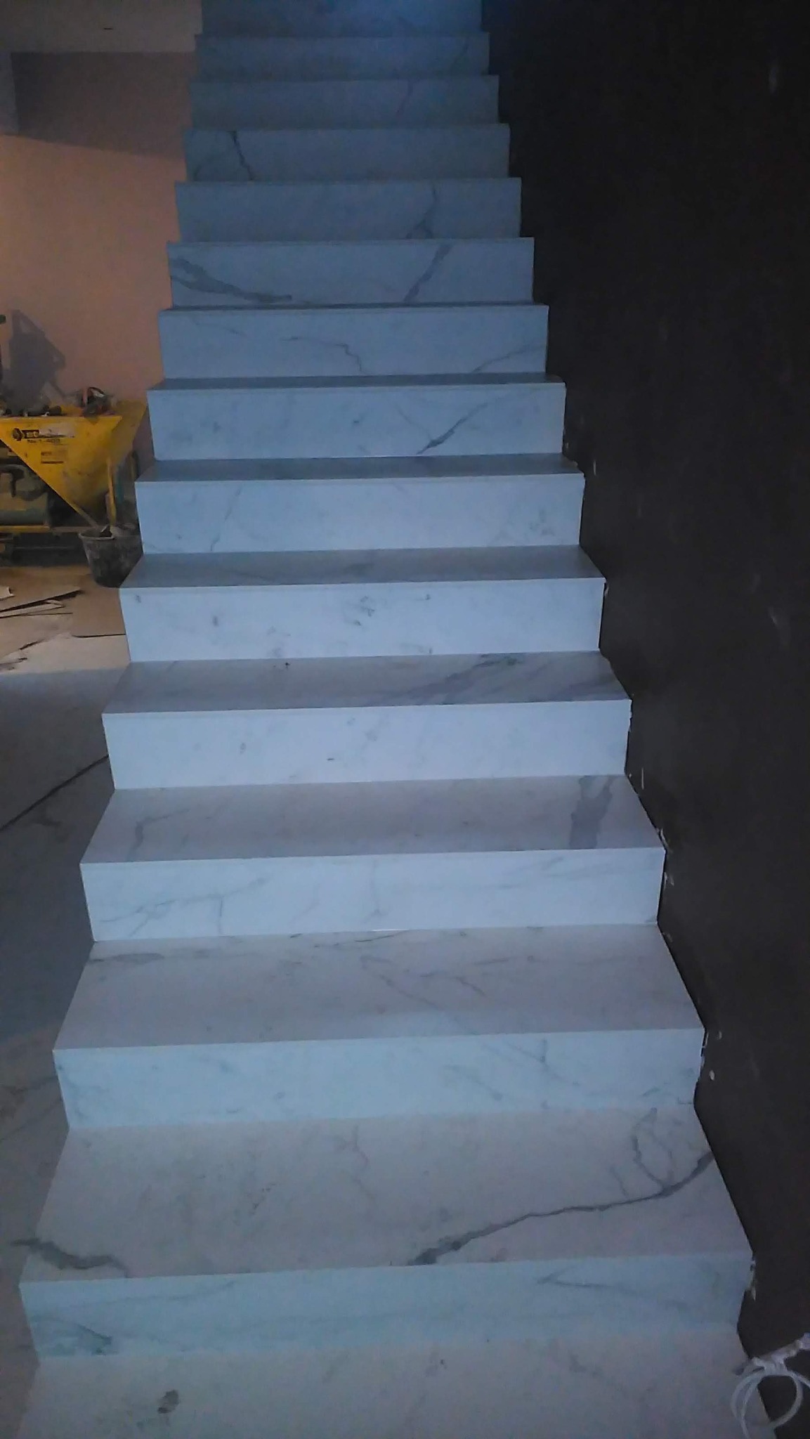 Schody wyłożone białym marmurem z szarymi żyłami, widoczne narzędzia i resztki zaprawy w tle.