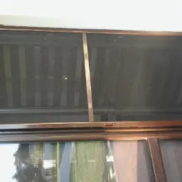 Zewnętrzna przesłona okienna z brązową ramą, widoczna od wewnątrz, z refleksami otoczenia w Pułtusku.